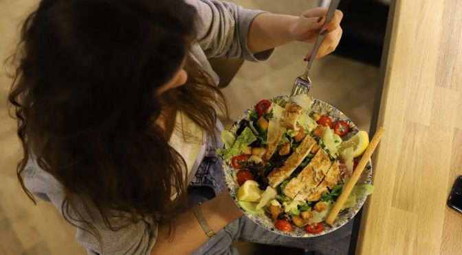 Overhead view of a woman eating a chicken salad balancing health with deliciousness.