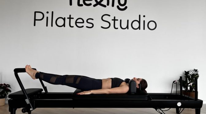 A woman performs exercises on a pilates reformer in a modern studio setting.